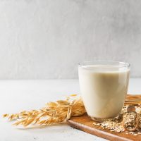 Oat milk in glass with flakes and spike or ears of grain on white background, copy space