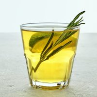 Glass cup of kombucha is decorated with rosemary and lime on a light gray concrete table. An invigorating low-alcohol carbonated drink on a hot day